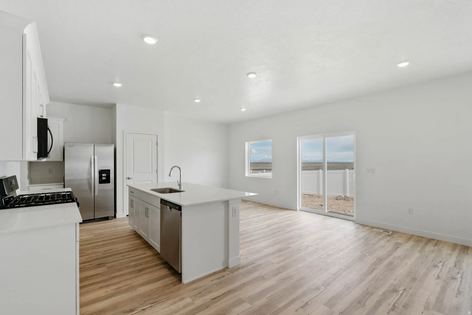 Open-concept living area featuring wood-finish flooring, white cabinetry, stainless steel appliances, and a kitchen island with sink