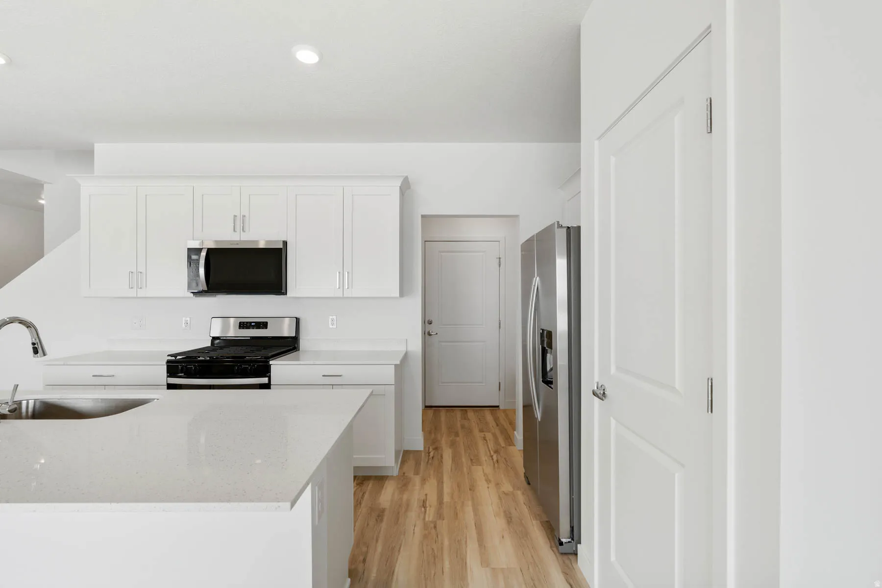 White cabinetry with crown molding, stainless steel appliances, quartz countertops, a kitchen island with sink, and wood-finish flooring