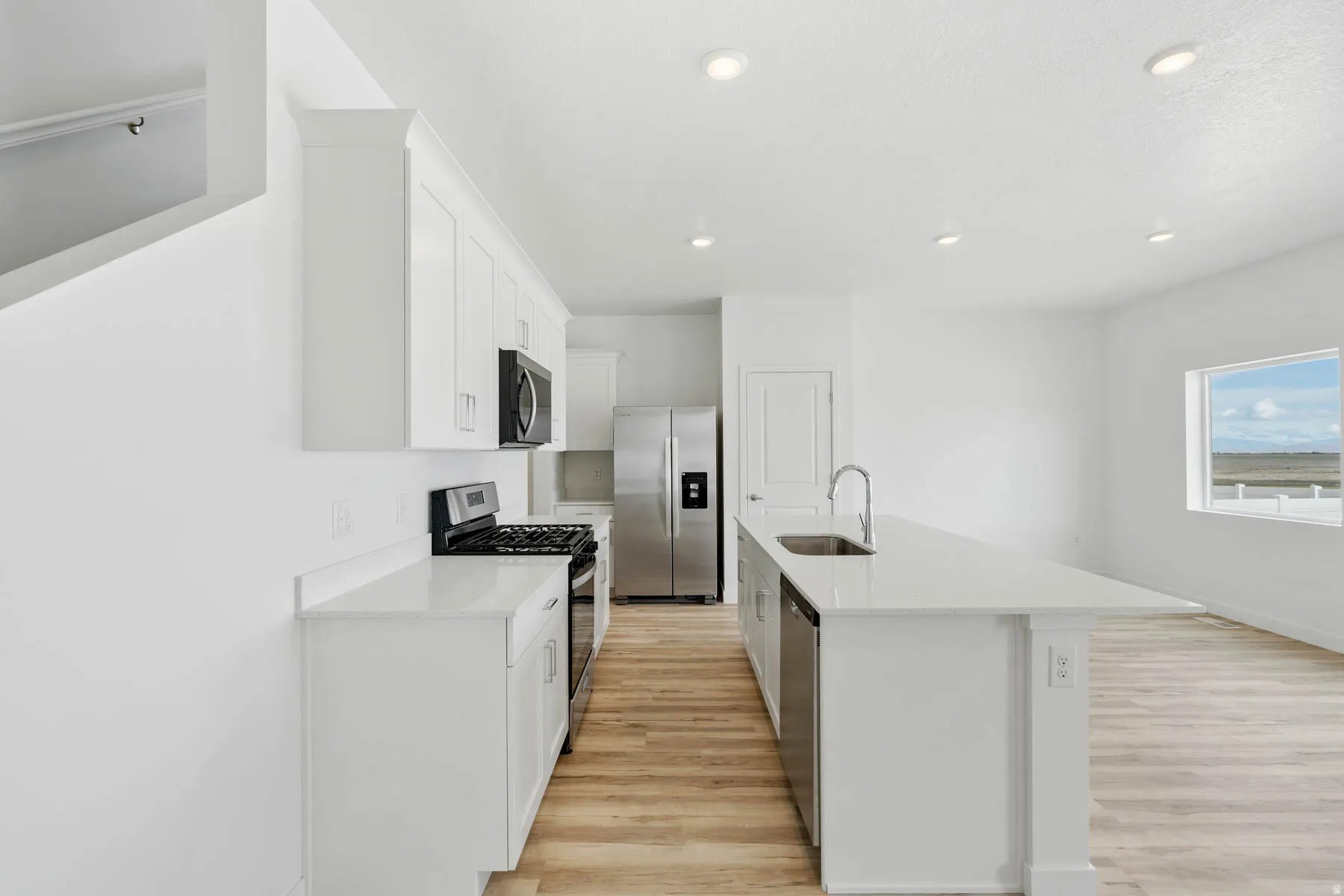 Kitchen featuring white cabinetry, stainless steel appliances, a center island with sink, light wood-finish flooring, and recessed lighting