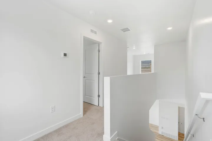 Recessed lighting throughout, white walls, and light-toned carpet flooring