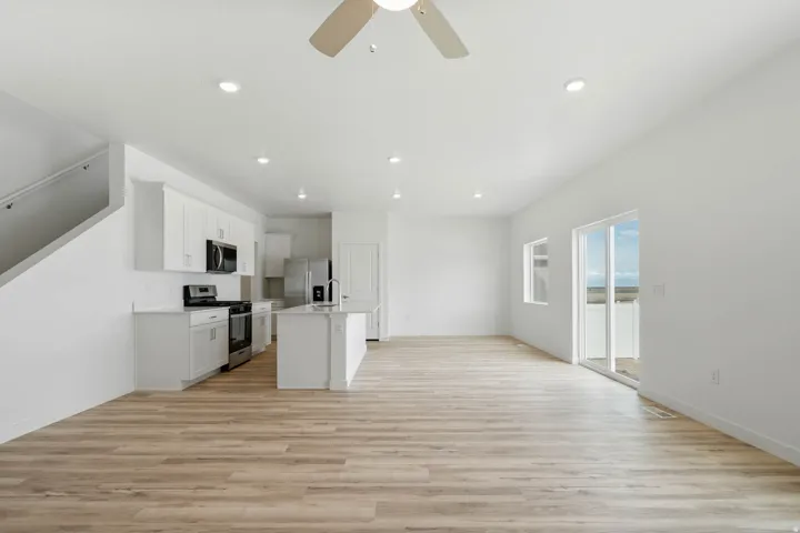 Open-concept living area with wood-finish flooring, white cabinetry, stainless steel appliances, and a kitchen island
