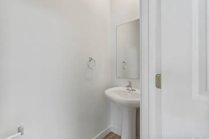 Pedestal sink with chrome faucet, wall-mounted mirror, and wood-finish flooring