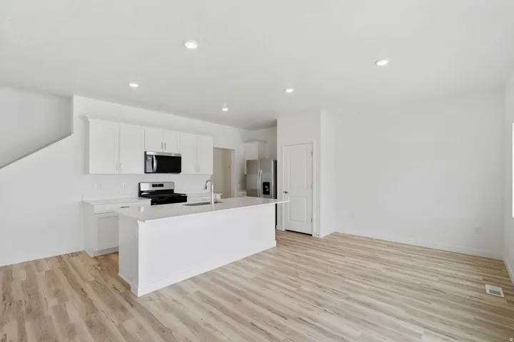 Open-concept living space with wood-finish flooring, recessed lighting, white cabinetry, and stainless steel appliances