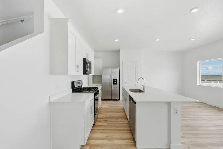 Kitchen featuring white cabinetry, stainless steel appliances, a center island with sink, light wood-finish flooring, and recessed lighting