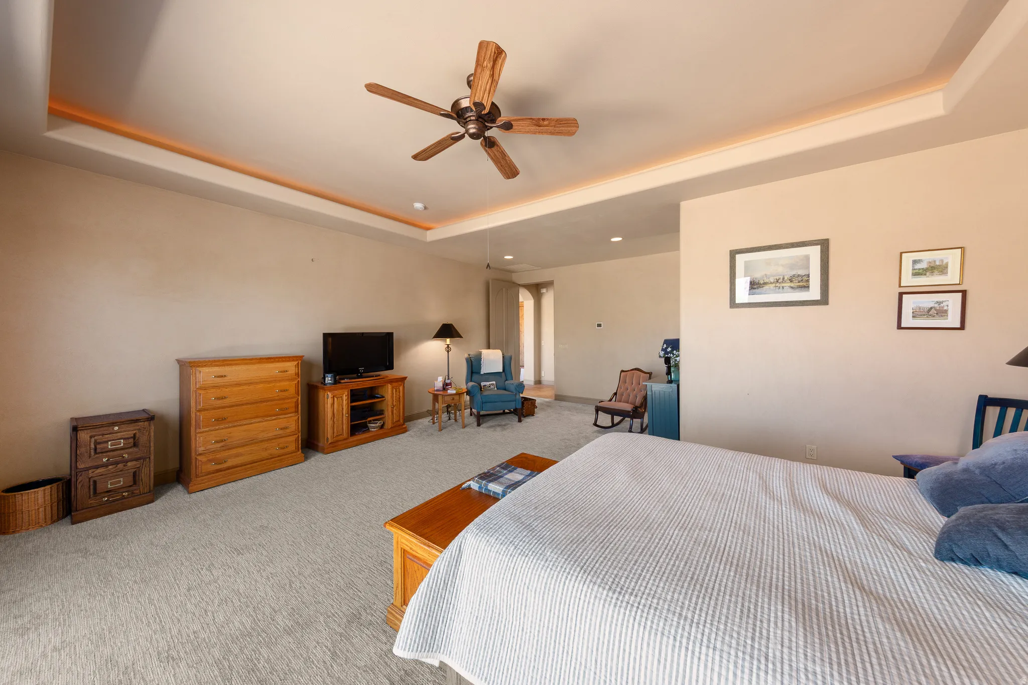 Tray ceiling with ambient lighting, wood-finish ceiling fan, and neutral tone carpeting