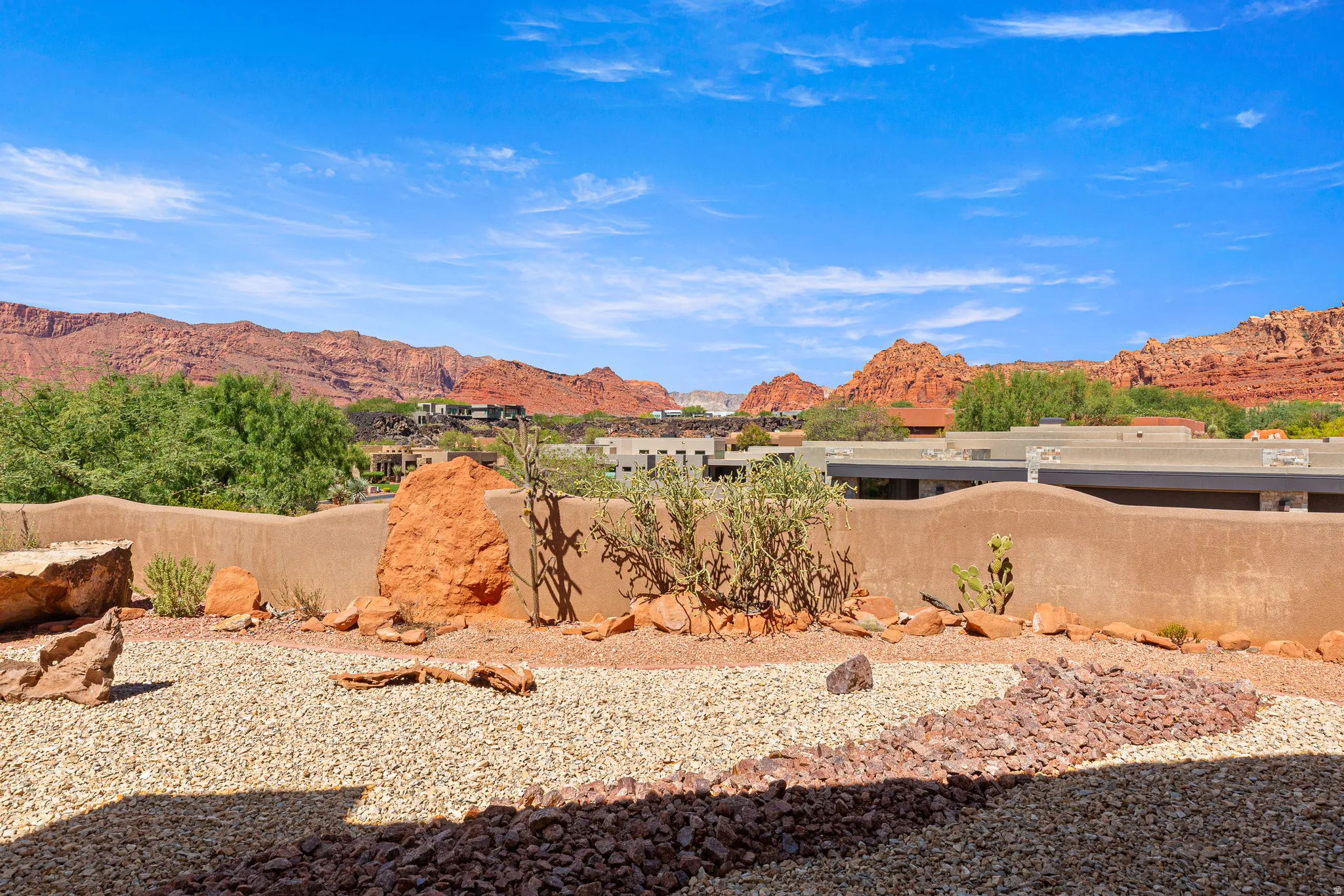 Desert landscaping with varied gravel beds and natural rock features, complemented by a low stucco wall