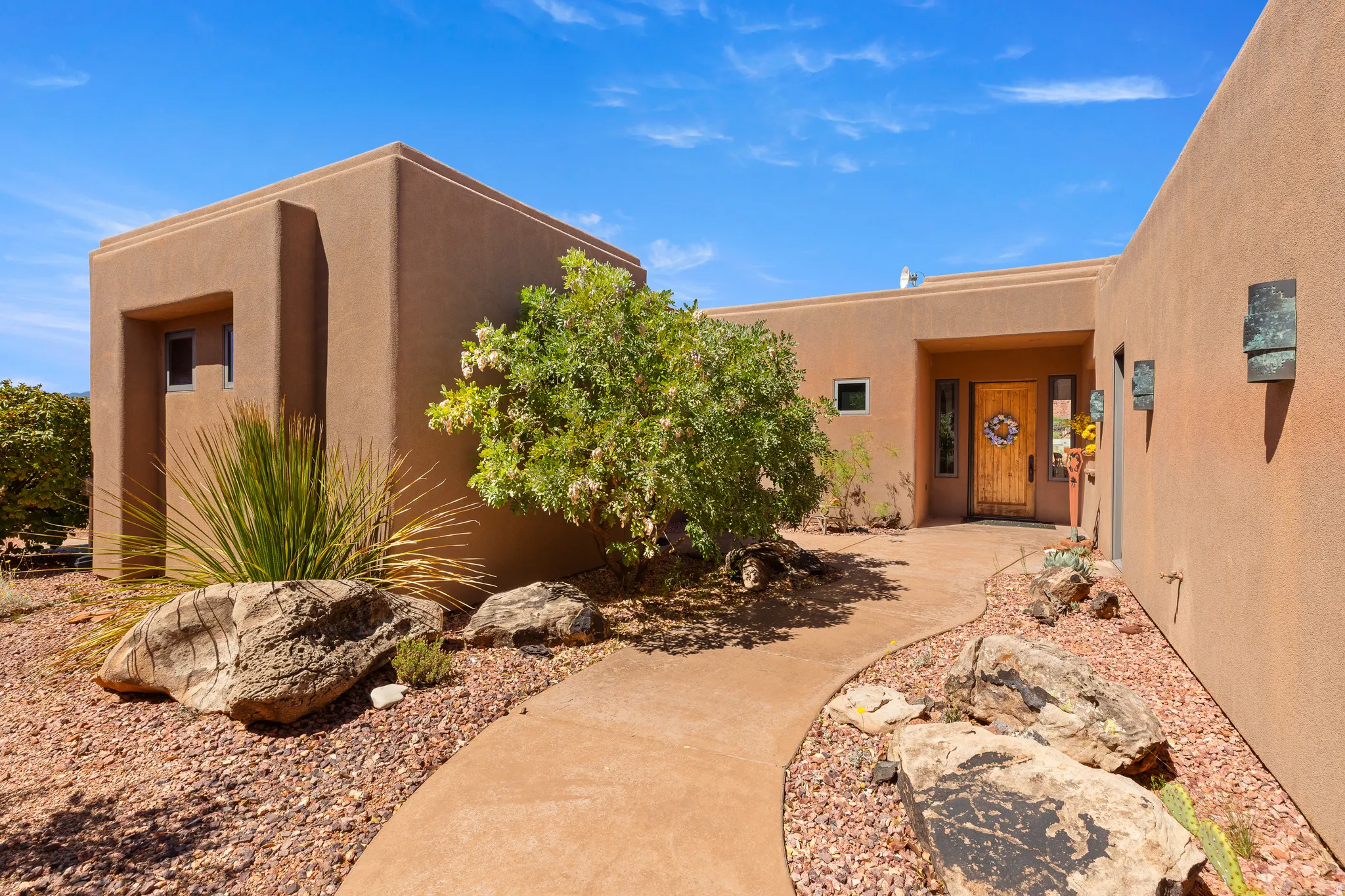 Smooth stucco exterior with a natural wood entry door, featuring a curved concrete pathway and rock landscaping