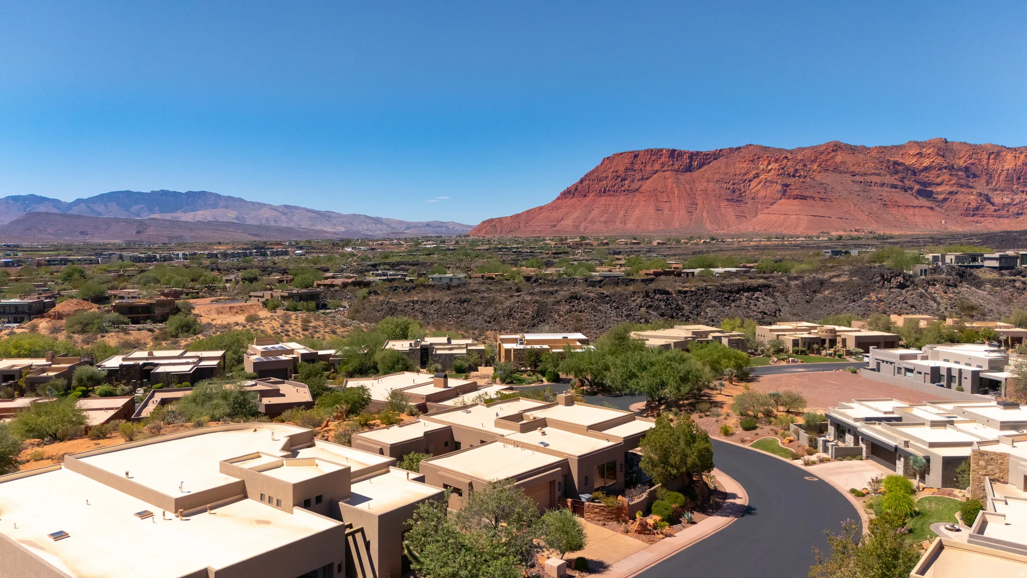 Expansive neighborhood featuring diverse architectural styles, mature landscaping, paved roadways, and prominent red rock mountain backdrop