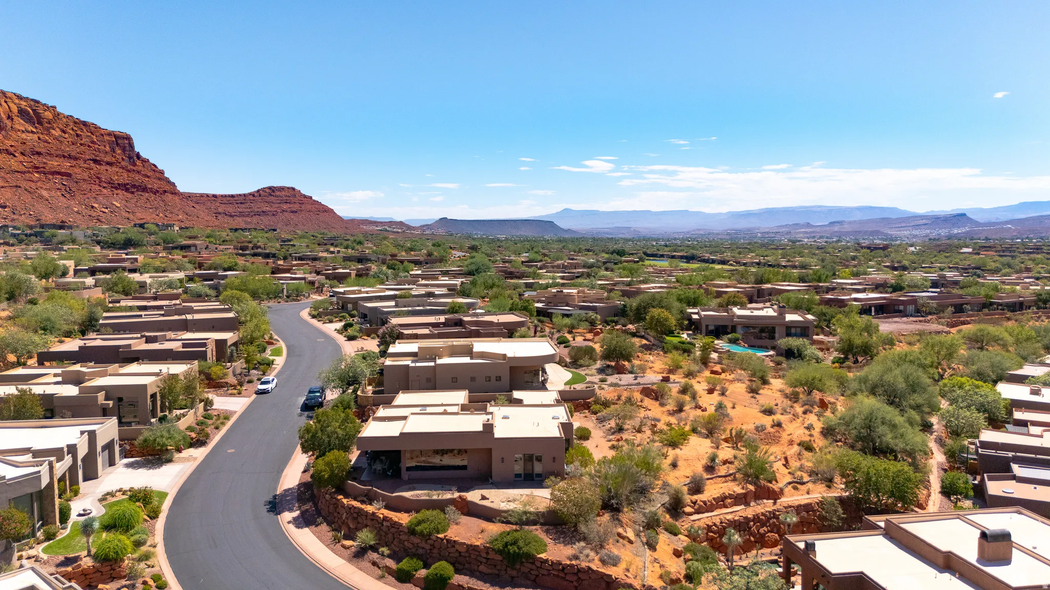 Aerial perspective showcasing a residential community with contemporary architecture, a winding paved road, and desert landscaping