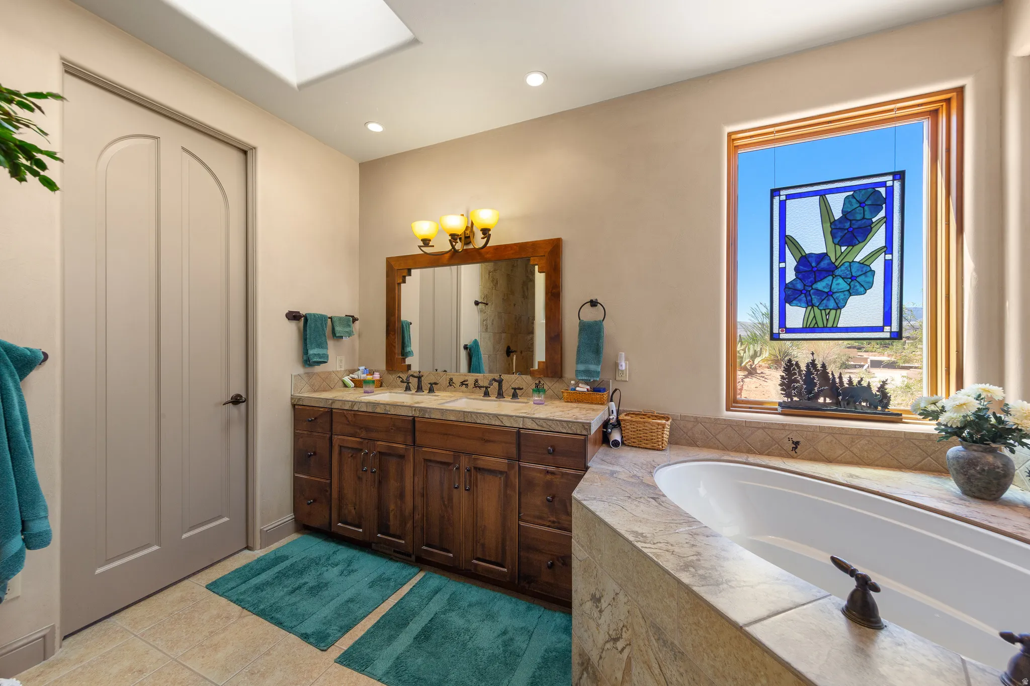 Bathroom featuring a built-in soaking tub, wood-finish double vanity with dual sinks, a large window with wood trim, and a skylight