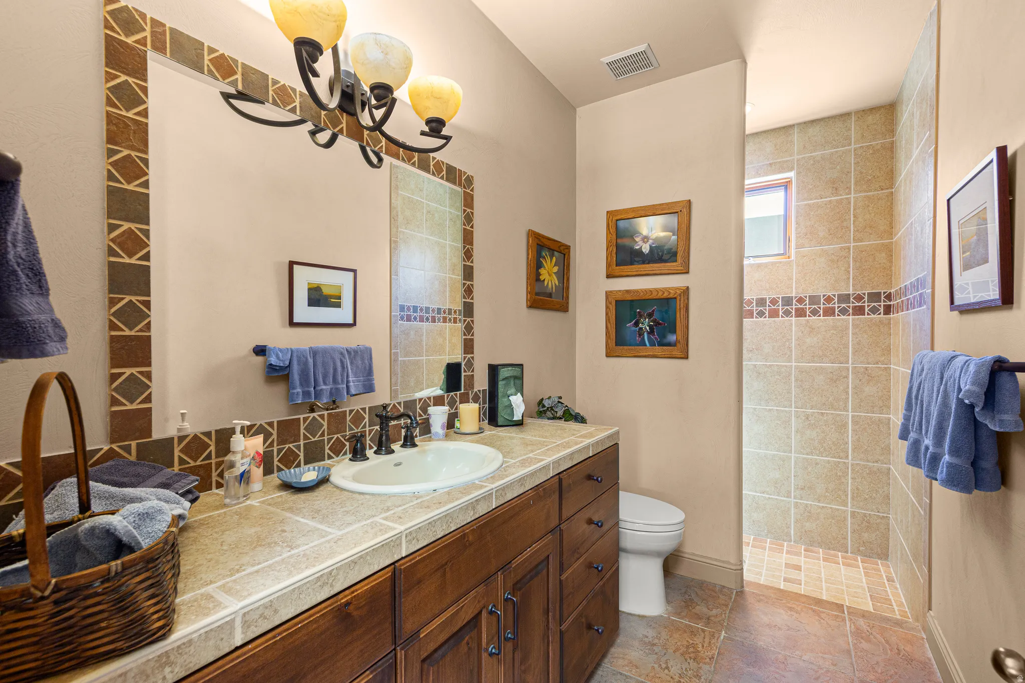 Vanity with integrated sink, tile countertop, dark wood-finish cabinetry, and a framed mirror