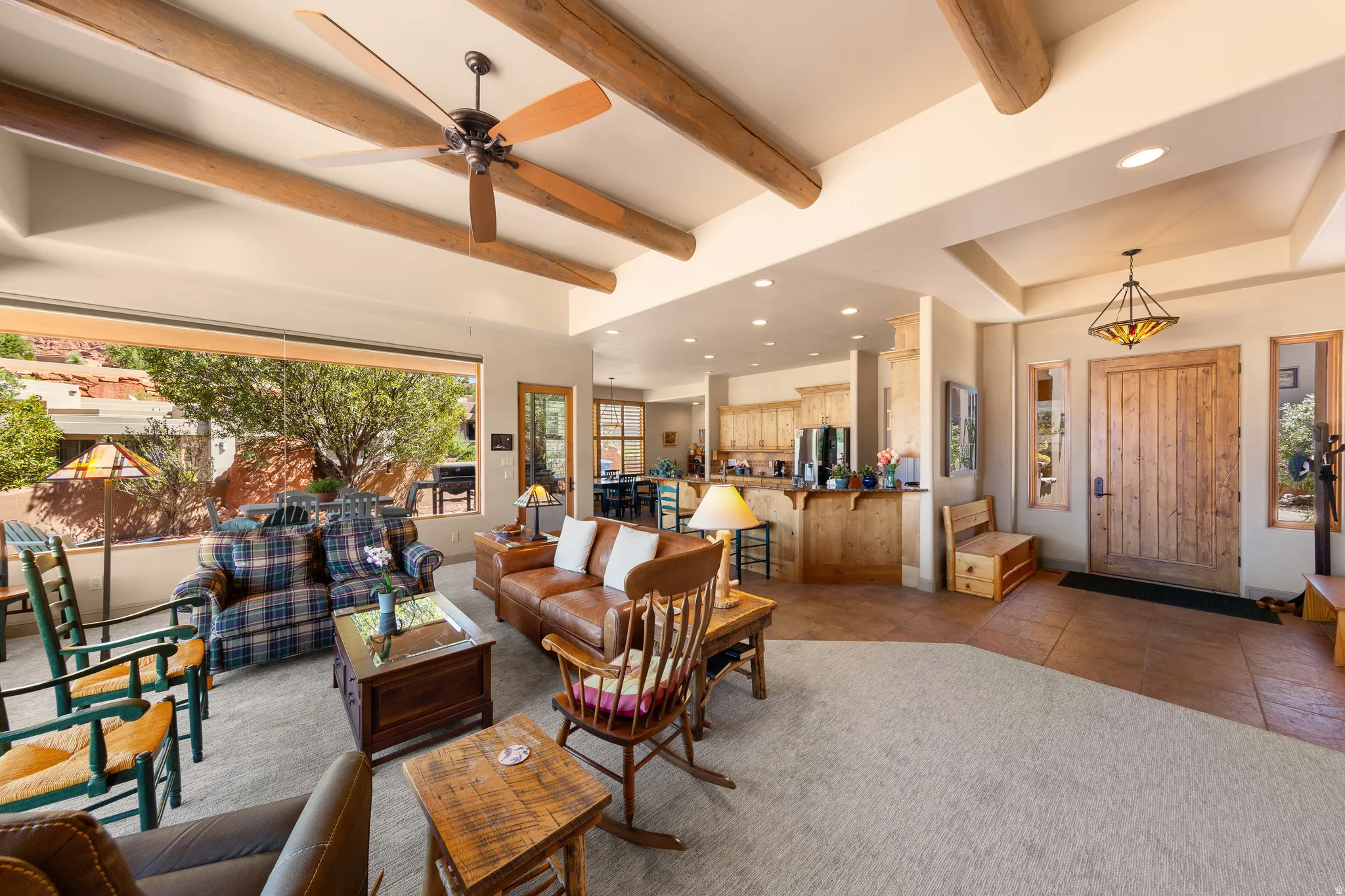 Exposed wood beam ceiling with recessed lighting, expansive window, wood-finish entry door with sidelights, and a kitchen featuring wood cabinetry and a breakfast bar
