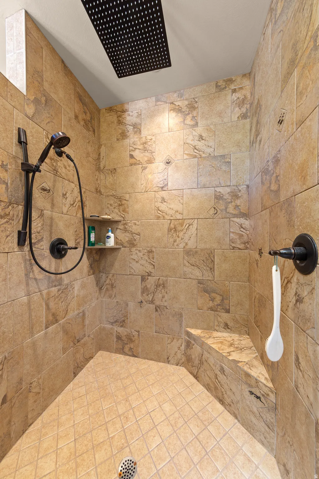 Tiled shower featuring a built-in bench, ceiling-mounted rainfall showerhead, handheld shower fixture, and a recessed shelf