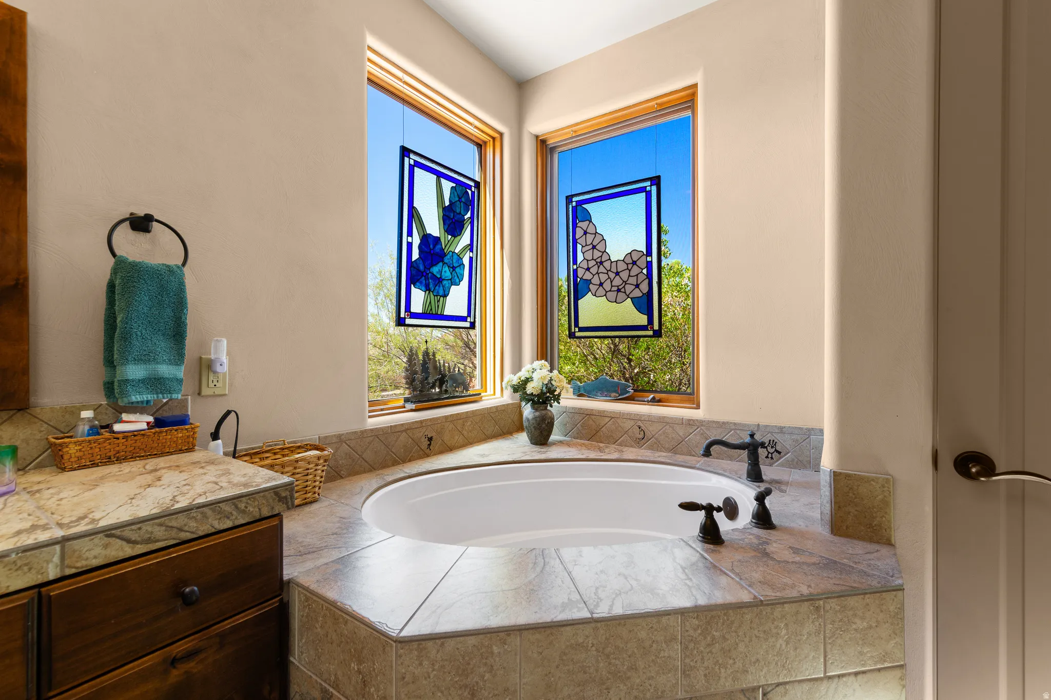 Built-in soaking tub with dark bronze fixtures, surrounded by tiled decking and backsplash