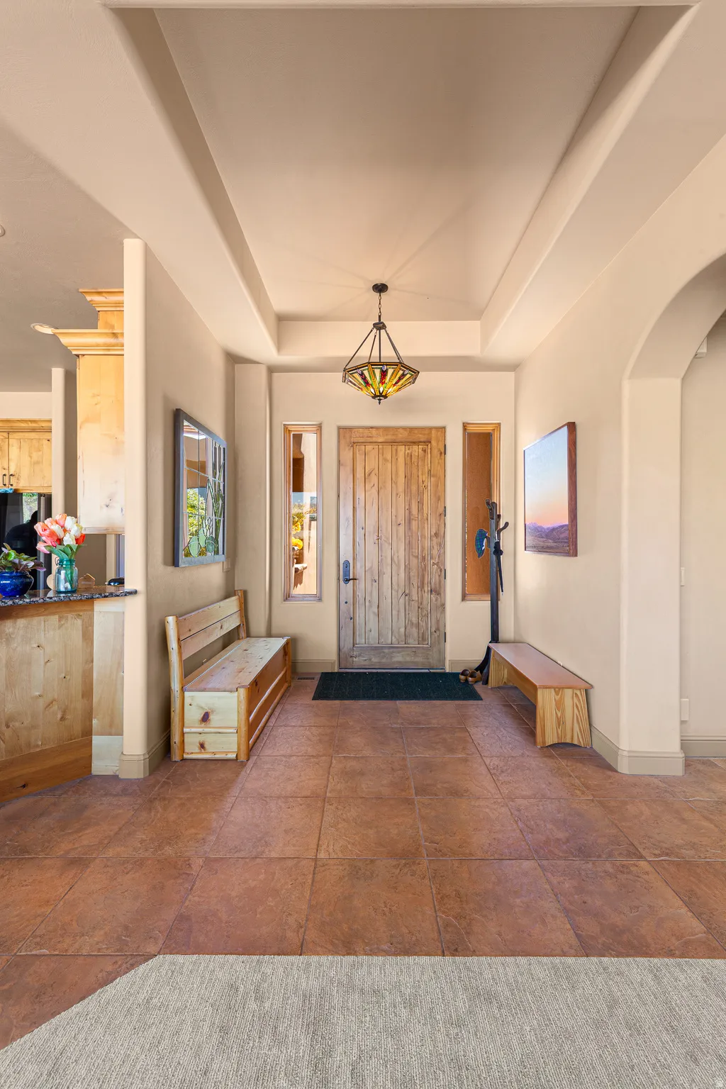 Entryway featuring a tray ceiling, a decorative pendant light fixture, a distressed wood-paneled door, and large square floor tiles