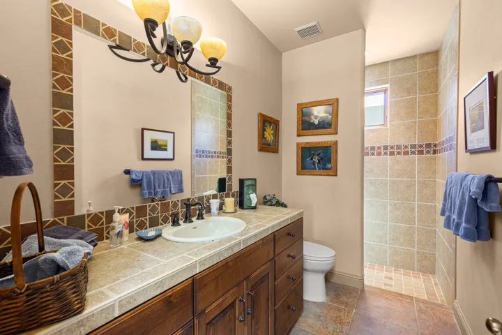 Vanity with integrated sink, tile countertop, dark wood-finish cabinetry, and a framed mirror