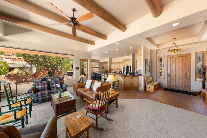 Exposed wood beam ceiling with recessed lighting, expansive window, wood-finish entry door with sidelights, and a kitchen featuring wood cabinetry and a breakfast bar