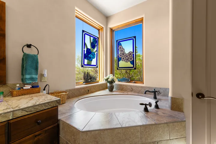 Built-in soaking tub with dark bronze fixtures, surrounded by tiled decking and backsplash