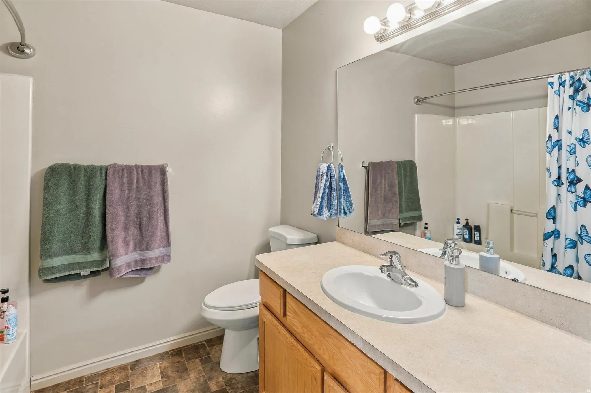 Bathroom featuring a single vanity with an integrated sink, wood-finish cabinetry, a full-width mirror, and a shower-tub combination