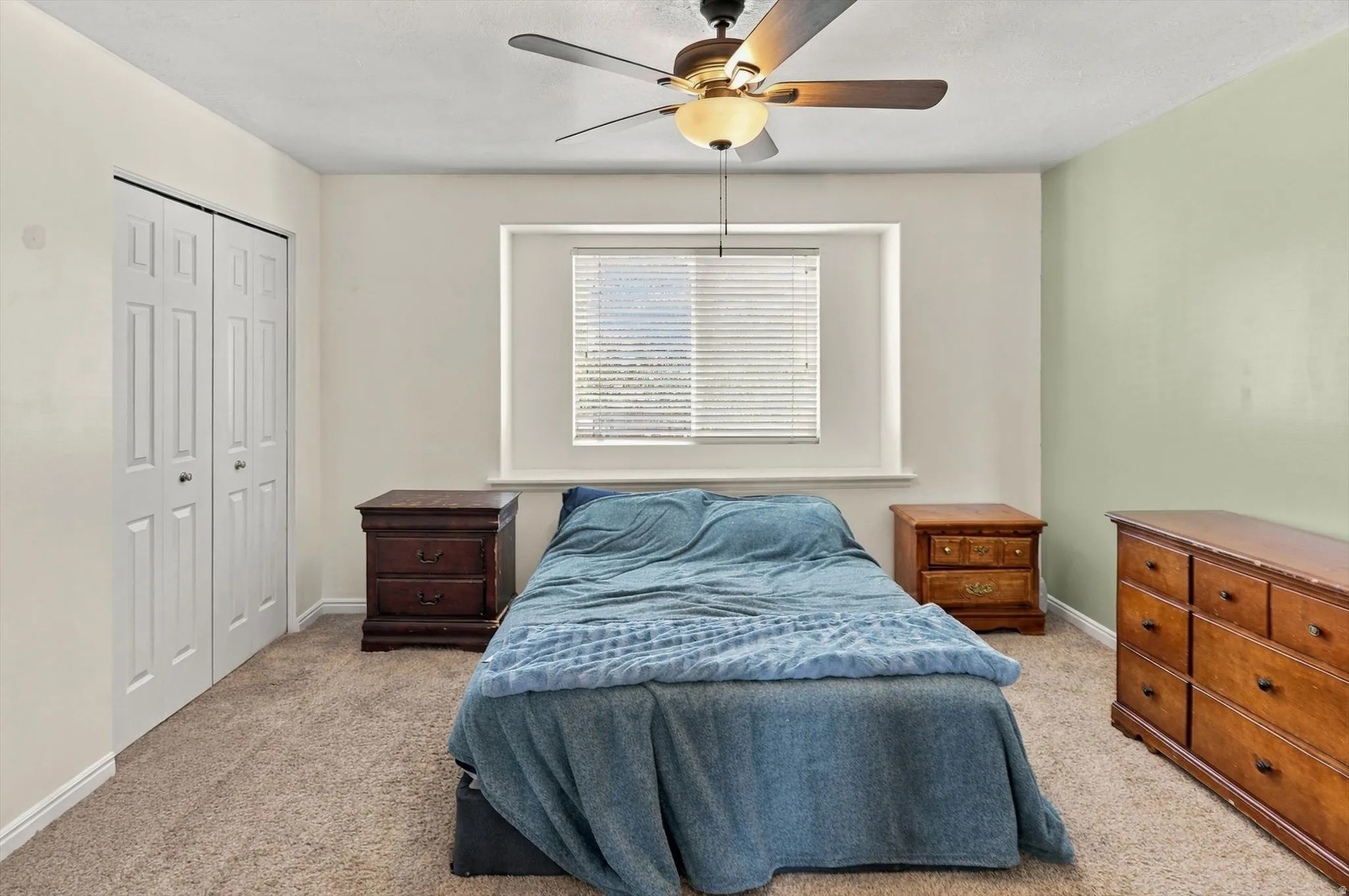 Carpeted room featuring a ceiling fan with integrated lighting, a window with blinds, and bi-fold closet doors