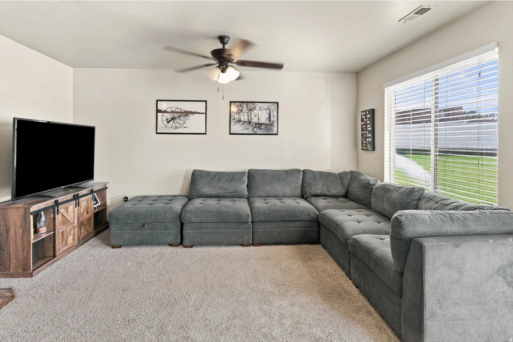 Carpeted living space with a ceiling fan, a large window, and light-toned walls