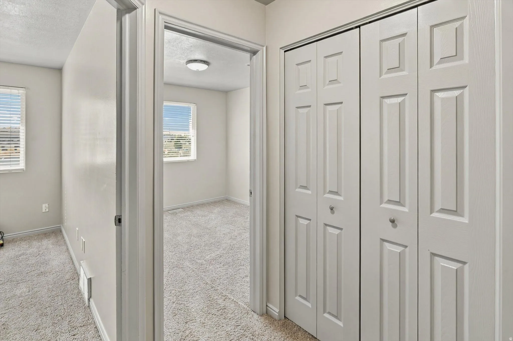 Bi-fold closet doors with panel detailing, neutral carpeting, and multiple windows with blinds