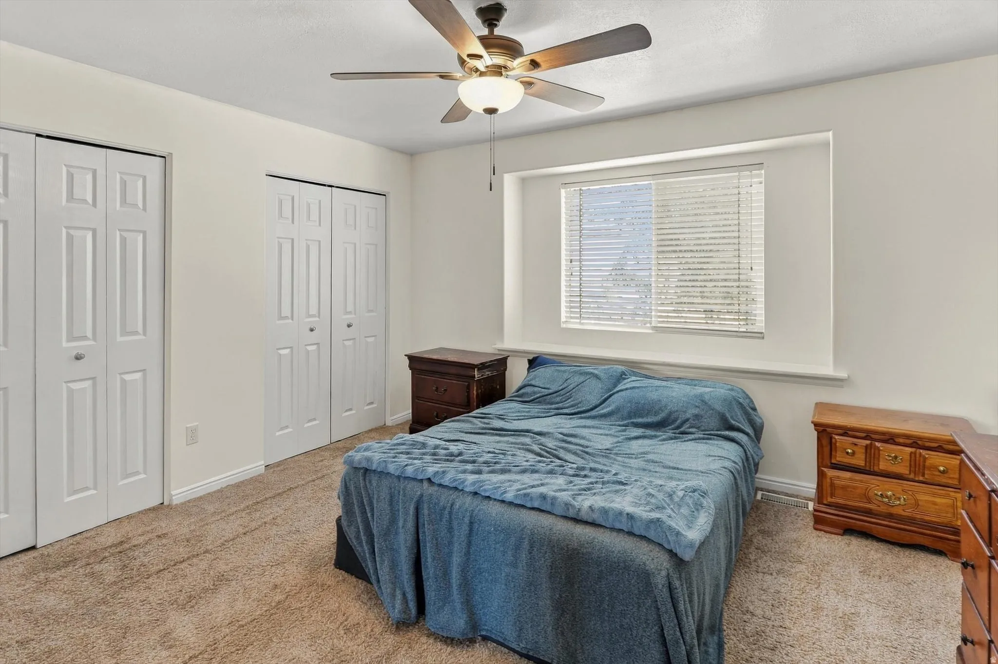 Window with blinds, wall-to-wall carpeting, two sets of bifold closet doors, and a ceiling fan with integrated lighting