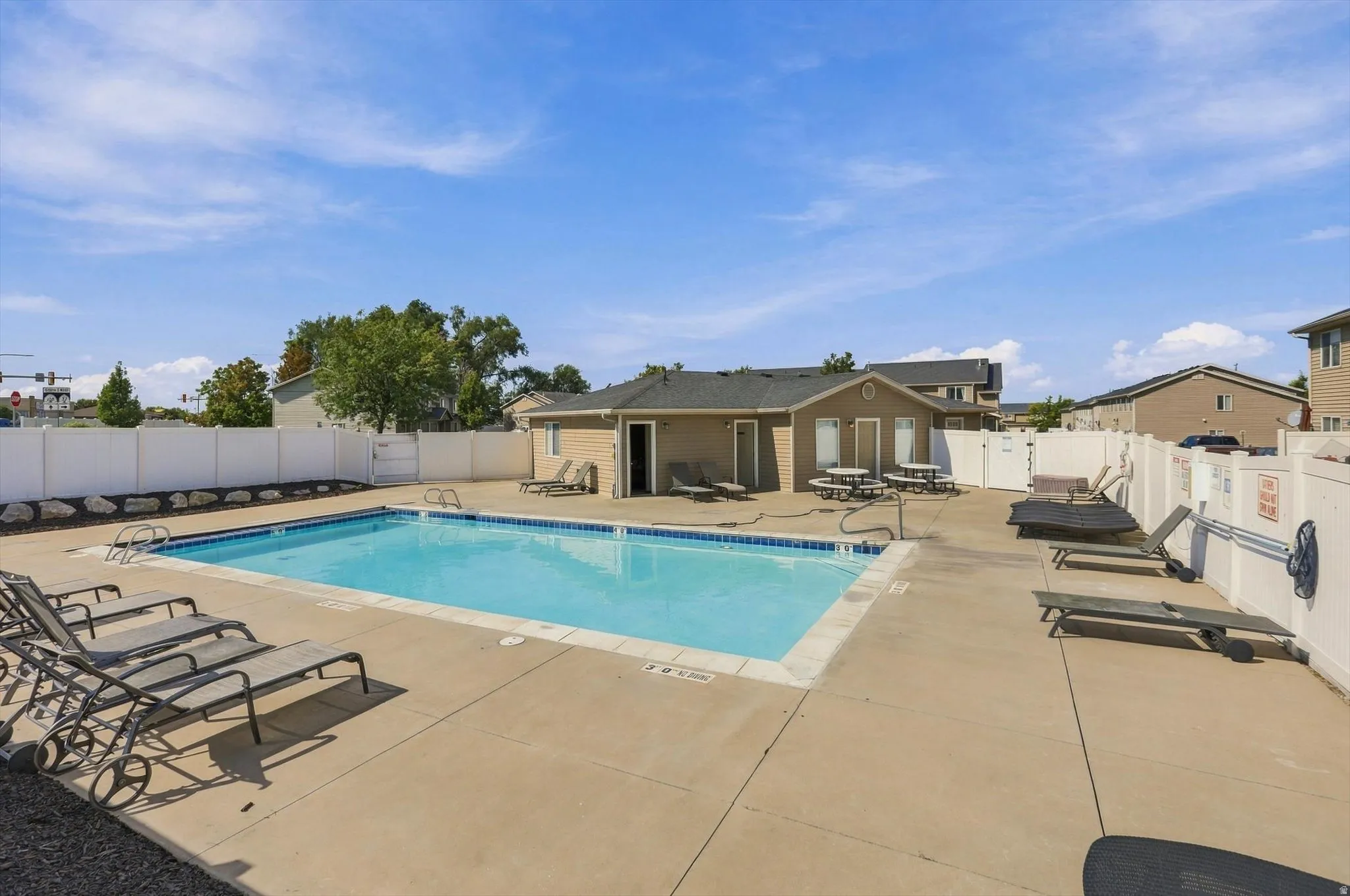Outdoor swimming pool with integrated steps, concrete surround, white privacy fencing, and an adjacent building