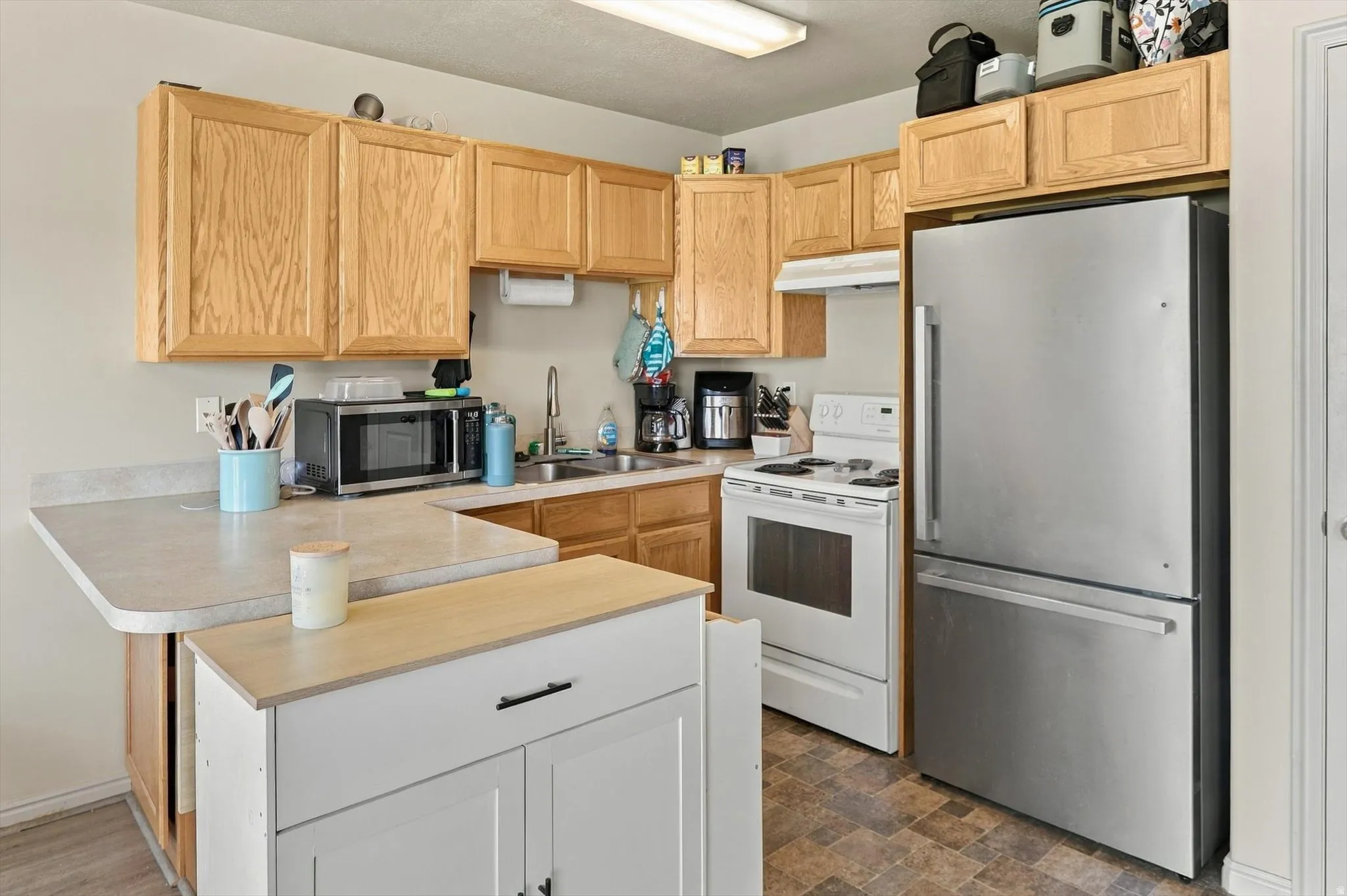 Kitchen featuring light wood cabinetry, light-toned countertops, a stainless steel refrigerator, and a white oven with an overhead microwave