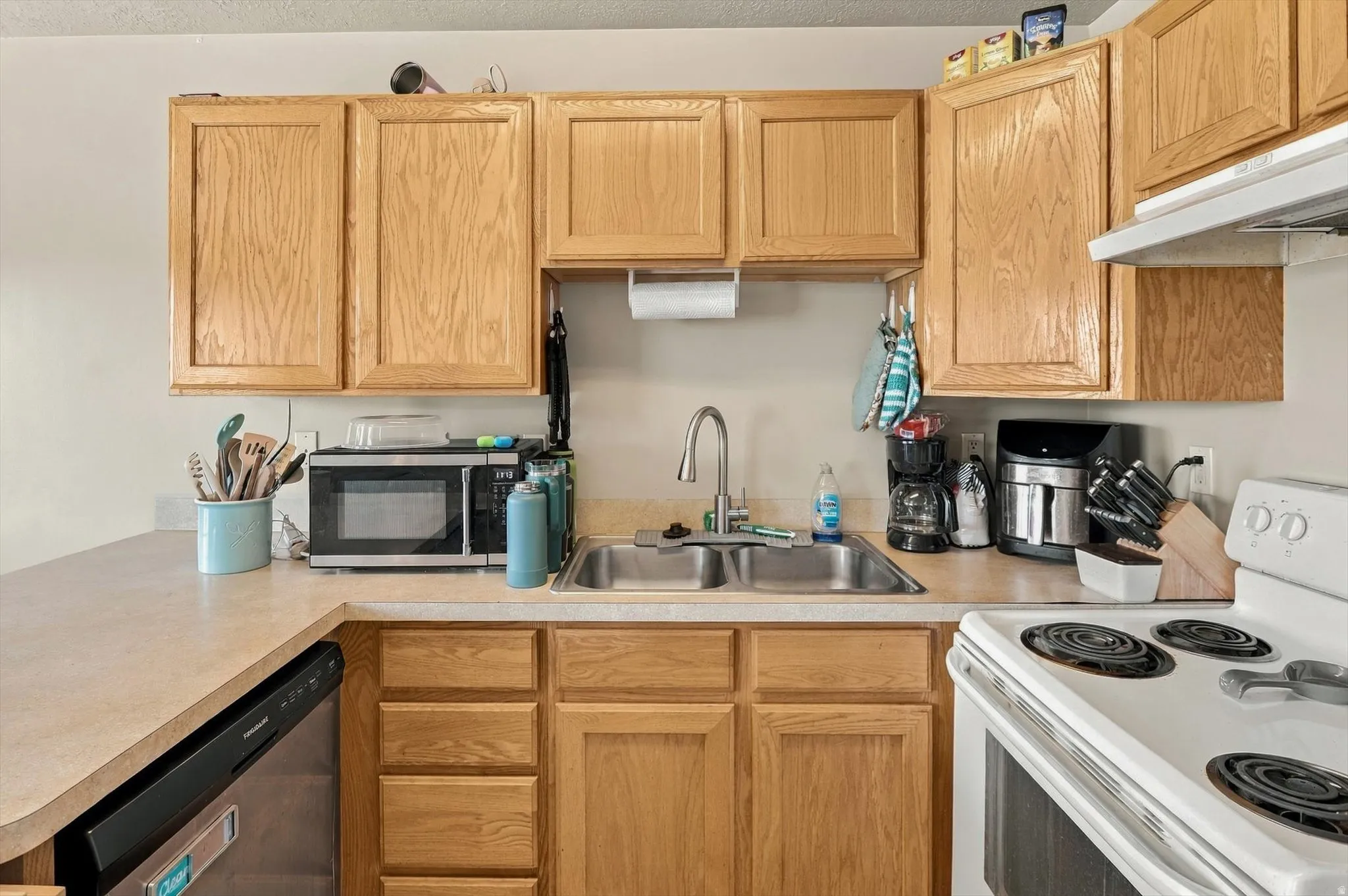 Kitchen featuring wood cabinetry, laminate countertops, a double-basin stainless steel sink, a built-in dishwasher, and an electric range with an overhead vent