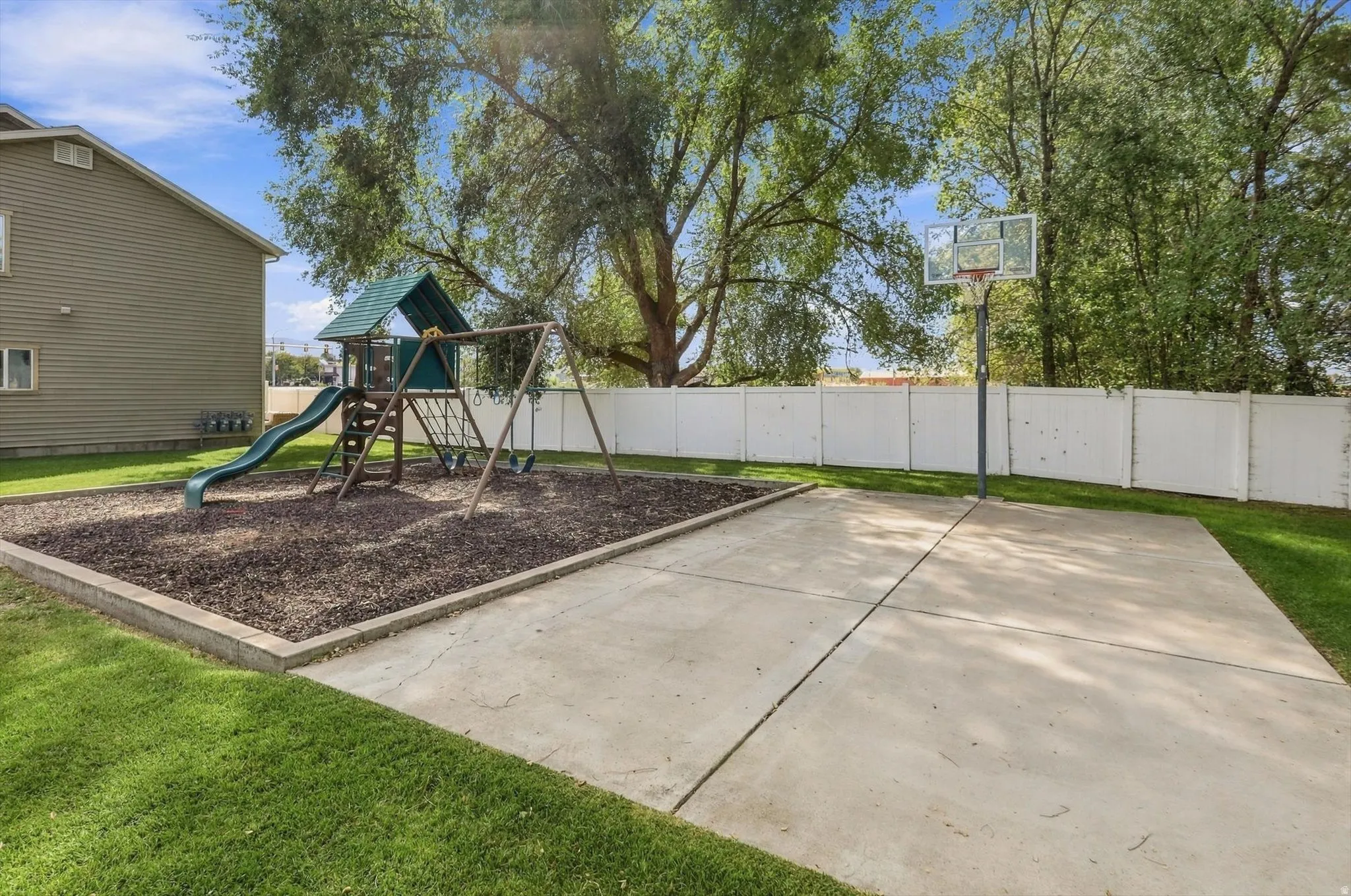 Expansive backyard featuring a dedicated play area with wood chip surfacing, a swing set, and a slide structure