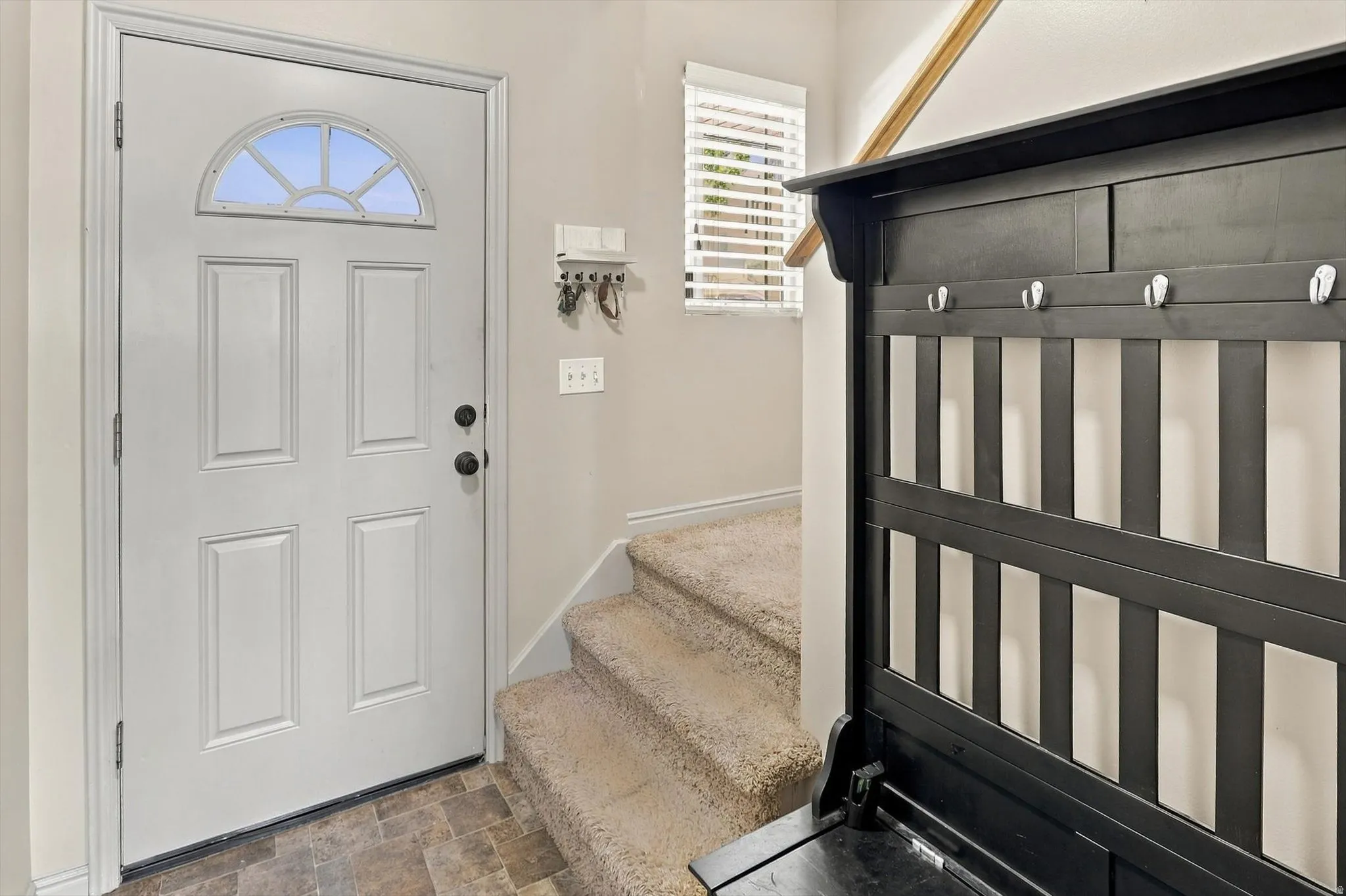 Entryway featuring a paneled door with an arched transom, durable tile-look flooring, and a carpeted staircase with a wood handrail