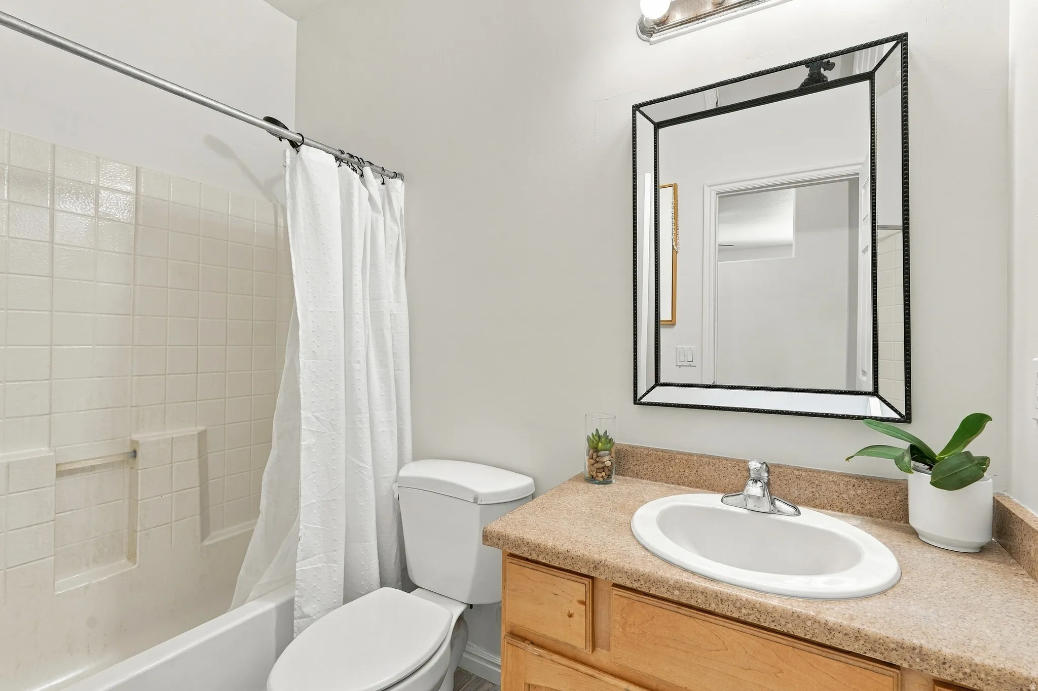 Bathroom featuring an integrated bathtub and shower, a white ceramic toilet, a vanity with a light-toned countertop, a rectangular mirror, and an overhead light fixture