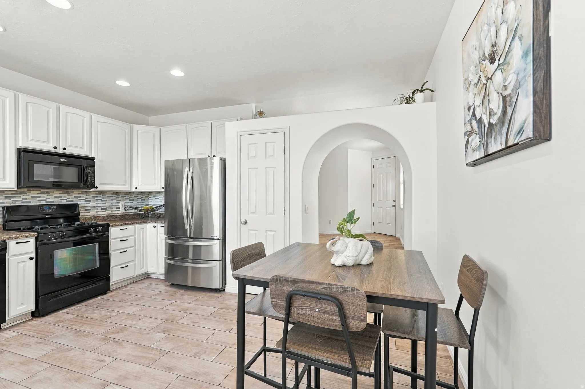 Kitchen featuring white cabinetry, a neutral-toned tile backsplash, stainless steel refrigerator, black range, and recessed lighting