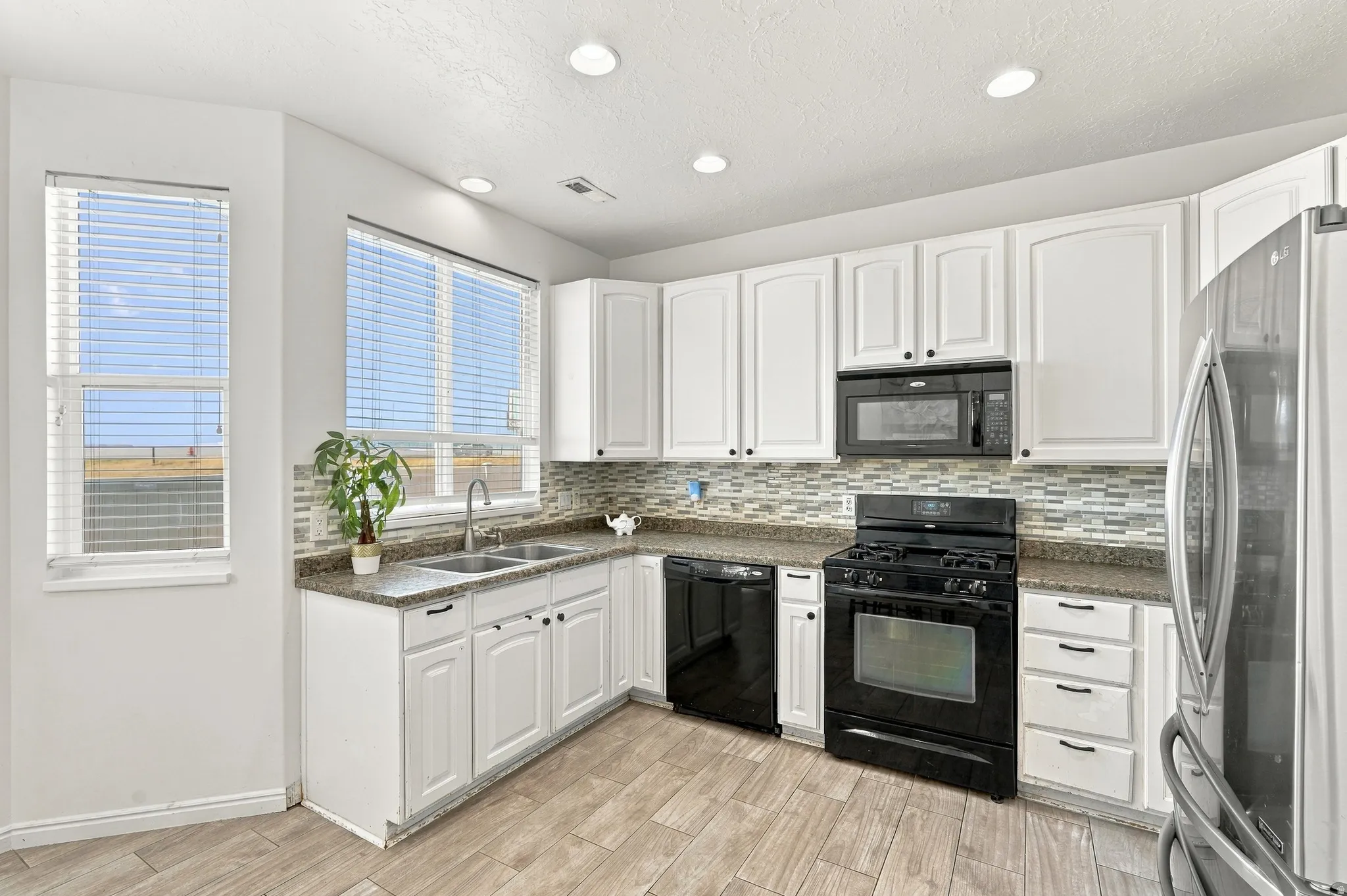 White cabinetry,  backsplash, stainless steel refrigerator, black range, and wood-finish flooring