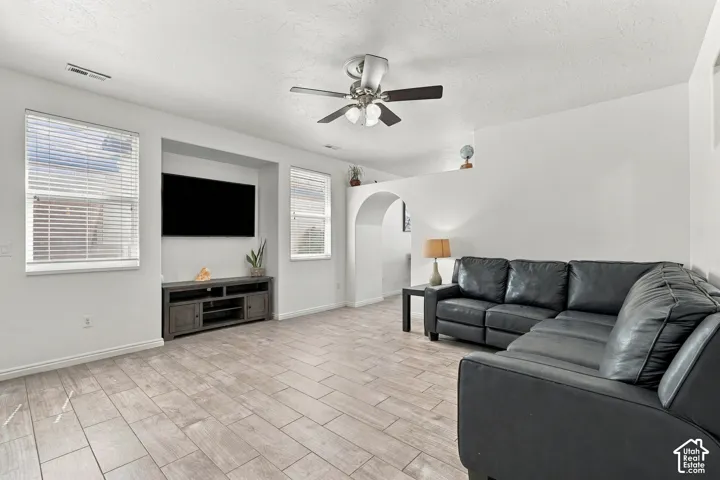 Wood-finish tile flooring, recessed media niche, multiple windows with blinds, ceiling fan with light, and arched doorway