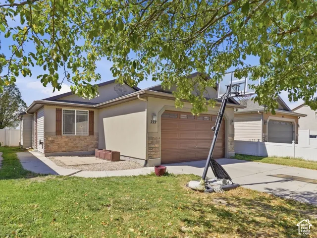 Stucco exterior with stone accenting, wood-look garage door, paved driveway, and established front lawn