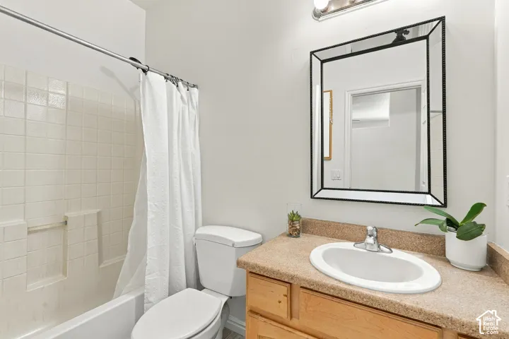 Bathroom featuring an integrated bathtub and shower, a white ceramic toilet, a vanity with a light-toned countertop, a rectangular mirror, and an overhead light fixture