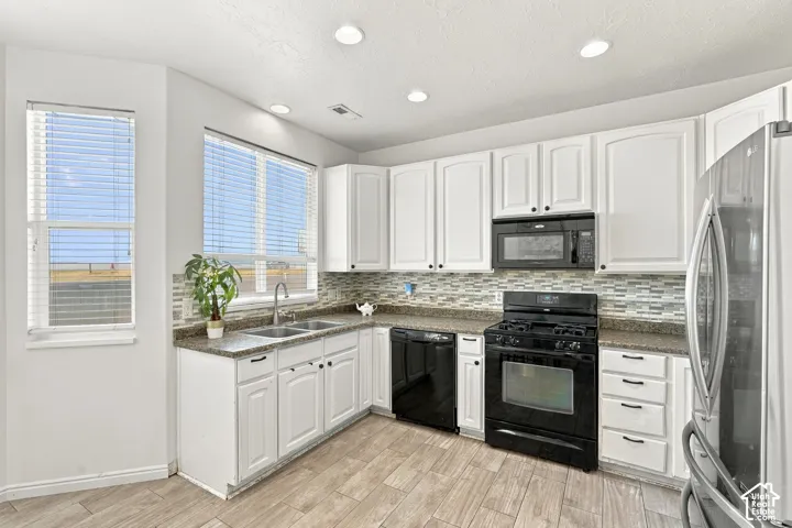 White cabinetry,  backsplash, stainless steel refrigerator, black range, and wood-finish flooring