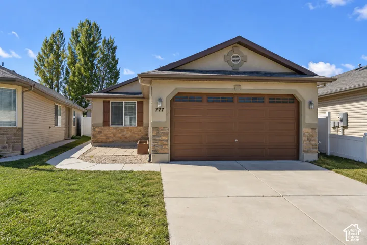 Single-story exterior featuring a stone and stucco facade, a concrete driveway, a panelled garage door, and a paver patio area