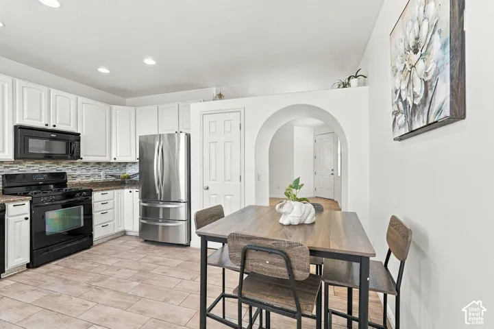 Kitchen featuring white cabinetry, a neutral-toned tile backsplash, stainless steel refrigerator, black range, and recessed lighting