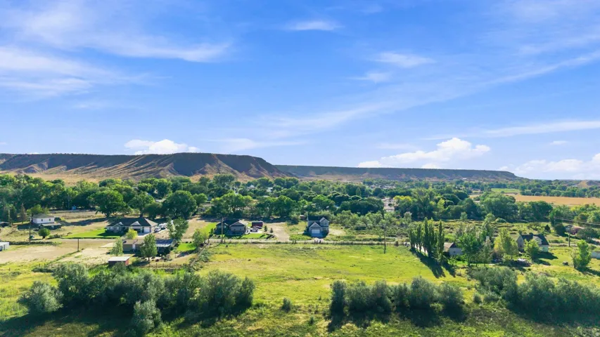 Expansive green landscape with scattered residential structures, mature trees, and distant mountain formations under a clear sky