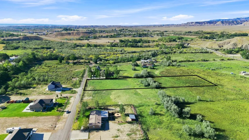 Expansive undeveloped land featuring a clear perimeter, established road frontage, surrounding mature trees, and distant mountainous terrain