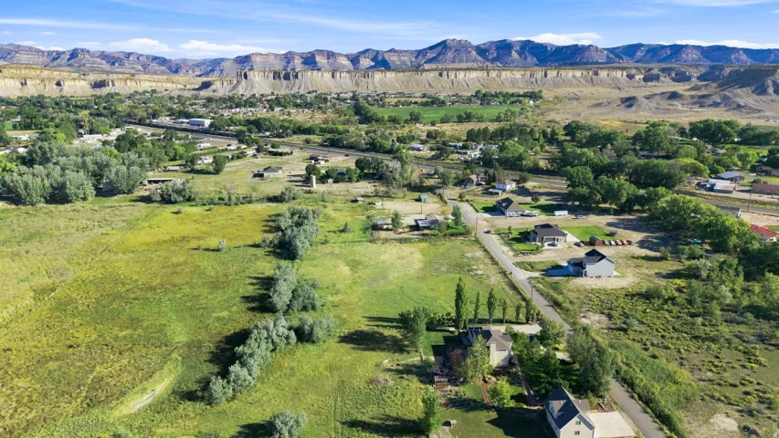Expansive rural landscape featuring a mix of green fields and scattered residential properties, bordered by distant mountain formations