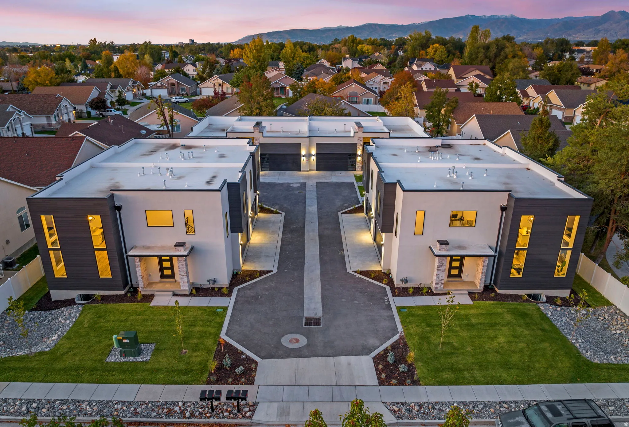 Modern architectural design with contrasting dark and light exterior panels, expansive flat rooflines, integrated two-car garages, and a paved central driveway