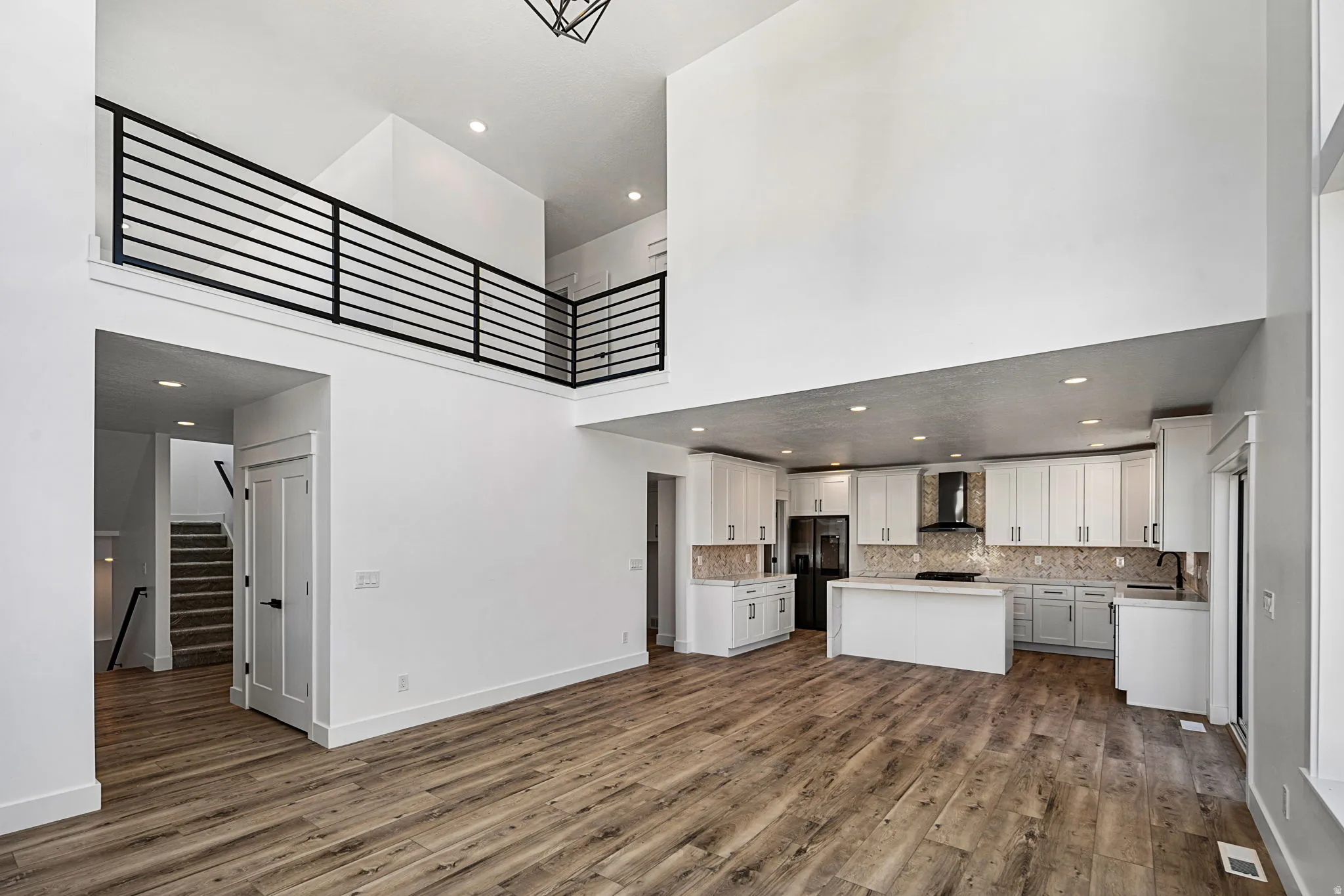 Vaulted ceilings with recessed lighting, wood-finish flooring, white cabinetry, a kitchen island, and a black range hood