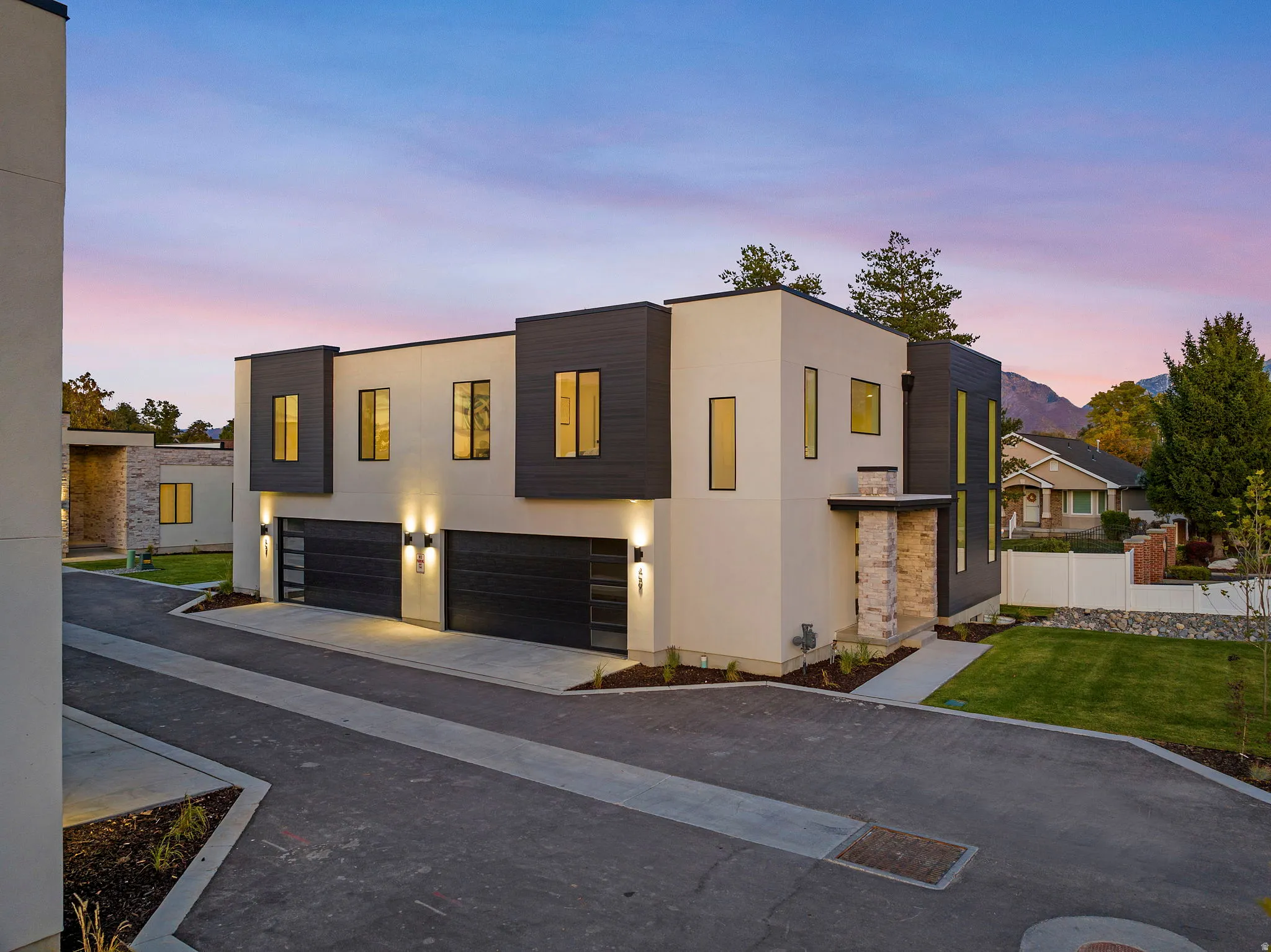 Contemporary facade with contrasting dark and light siding, multiple large windows, attached two-car garages, and stone accents