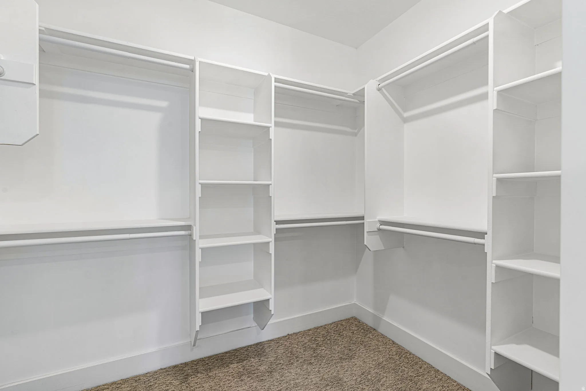 White shelving units, multiple hanging rods, built-in shelving, carpet flooring