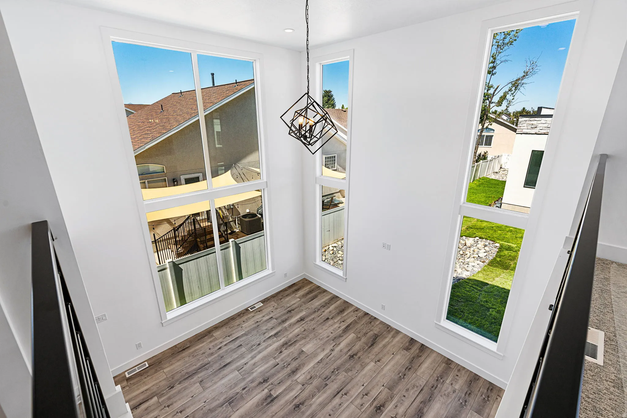 Double-height space featuring large windows, wood-finish flooring, and a contemporary light fixture