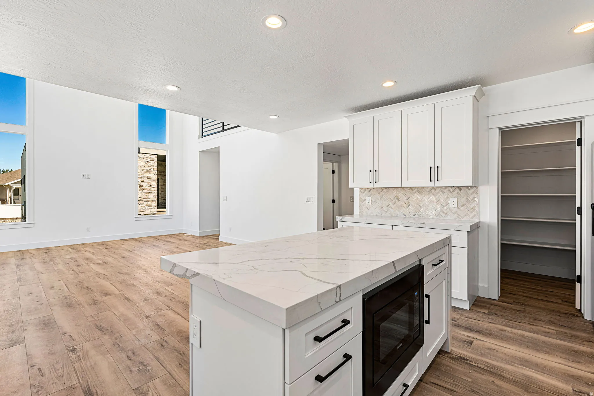 Kitchen island with a light-toned countertop, white cabinetry with black hardware, and wood-finish flooring